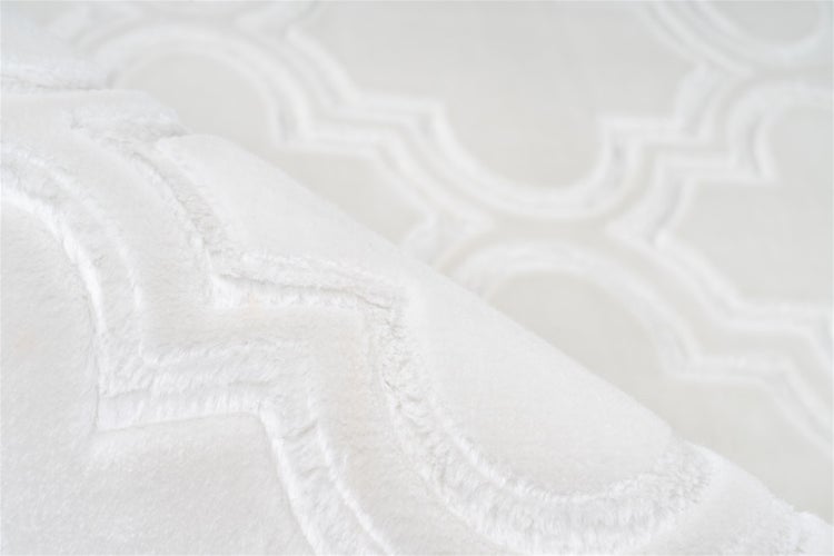 Nahaufnahme eines hochflorigen Teppichs mit geprägtem geometrischem Ornamentmuster und weicher Textur.