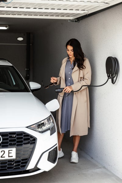 Frau lädt ein Elektroauto an einer wandmontierten Ladestation in einer Garage auf.