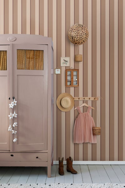Zimmer mit gestreifter Tapete, Kleiderschrank, Accessoires und Kinderkleidung für eine ordentliche, helle Atmosphäre.