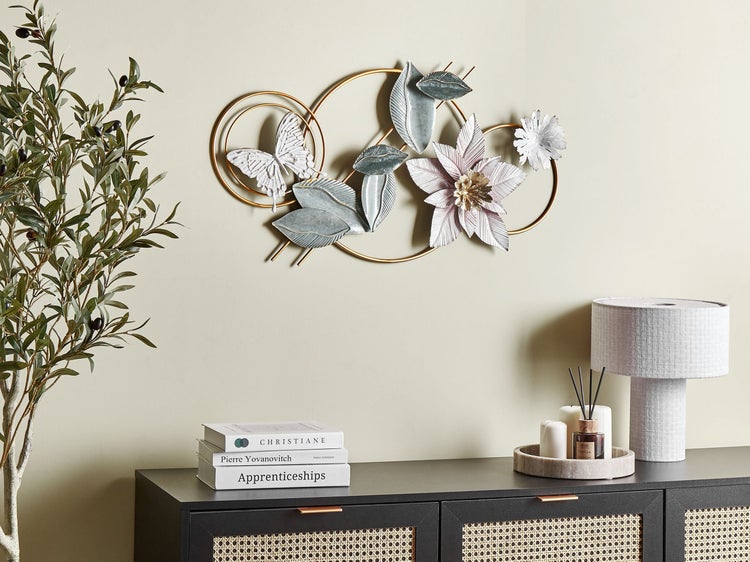 Dekorative Wanddekoration mit Blumen, Blättern und Schmetterling über einer Kommode mit Lampe und Büchern