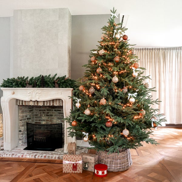 Festlich geschmückter Weihnachtsbaum mit Beleuchtung und Kugeln neben Kamin