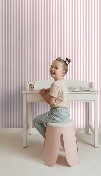 Mädchen sitzt an einem Schreibtisch vor einer gestreiften Tapete