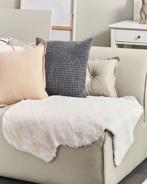 Dekoratives Wohnzimmer mit Kissen und Kunstfelldecke auf dem Sofa.