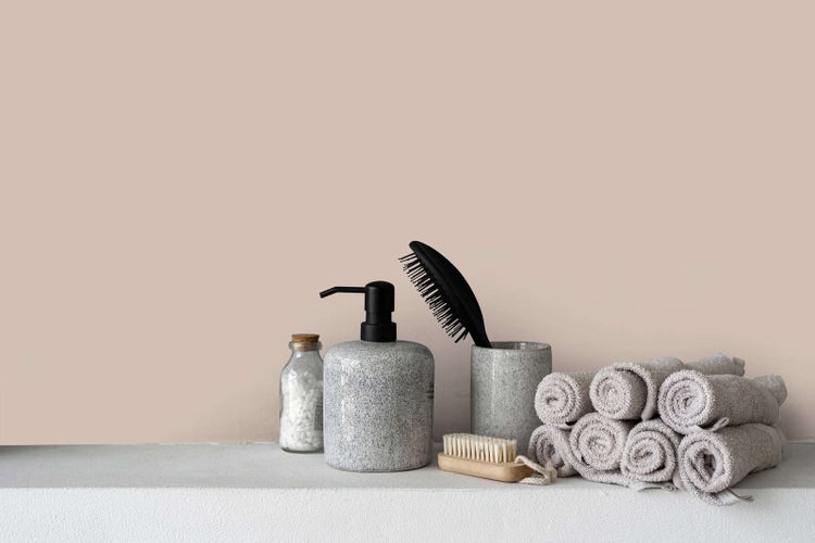 Wandfarbe in Beige hinter Badezimmer-Accessoires wie Seifenspender, Bürsten und gerollten Handtüchern auf einer Ablage.