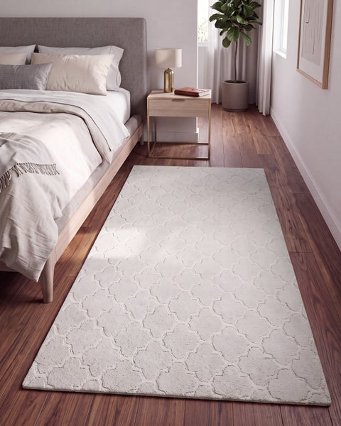 Ein moderner Schlafzimmerteppich mit orientalischem Muster liegt vor einem Bett auf einem Holzboden in einem hellen und gemütlichen Schlafzimmer.