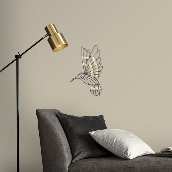 Wanddekoration Kolibri aus schwarzem Metall und hellem Seil, angebracht über einem grauen Sessel neben einer goldenen Stehlampe.
