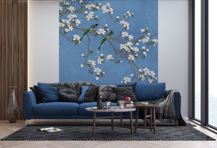 Wohnzimmer mit blauem Sofa und einer Tapete mit Vogel- und Blütenmuster