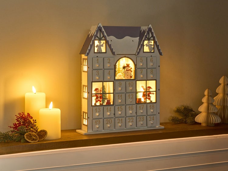 Beleuchteter Haus Adventskalender mit 24 Türchen, neben Kerzen und Dekoration