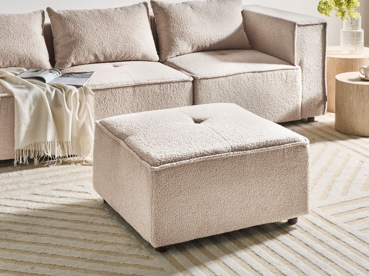 Quadratischer Polsterhocker aus Teddy-Stoff mit passendem Sofa in einem hellen Wohnzimmer.