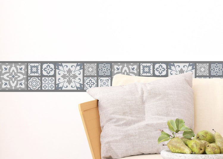 Selbstklebende Tapetenbordüre mit grauem orientalischem Fliesenmuster auf einer weißen Wand über einem Sofa.