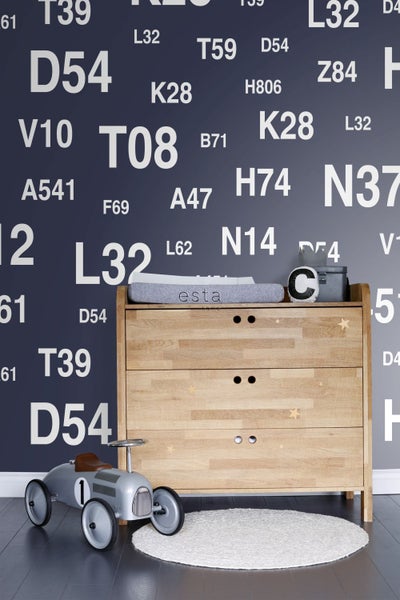 Holzkommode mit Wickelaufsatz, Spielzeugauto und Teppich in einem Kinderzimmer mit beschrifteter Wand