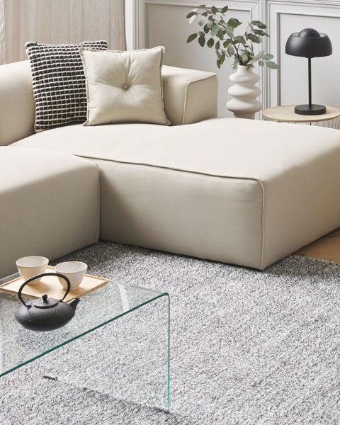 Helles Wohnzimmer mit modularem Sofa, Kissen, Teekanne und Glas Couchtisch