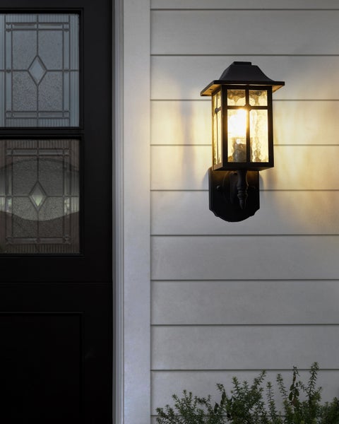 Eine schwarze Außenwandleuchte mit Laternenstil neben einer Tür.