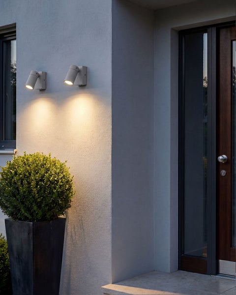 Zwei moderne Außenwandleuchten mit gerichteter Lichtausstrahlung an einer Hausfassade neben einer Eingangstür mit Buchsbaumkugel im Kübel.