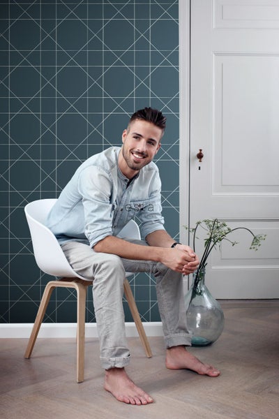 Wohnszene mit einem Mann auf einem Stuhl vor einer Wand mit geometrischer Tapete