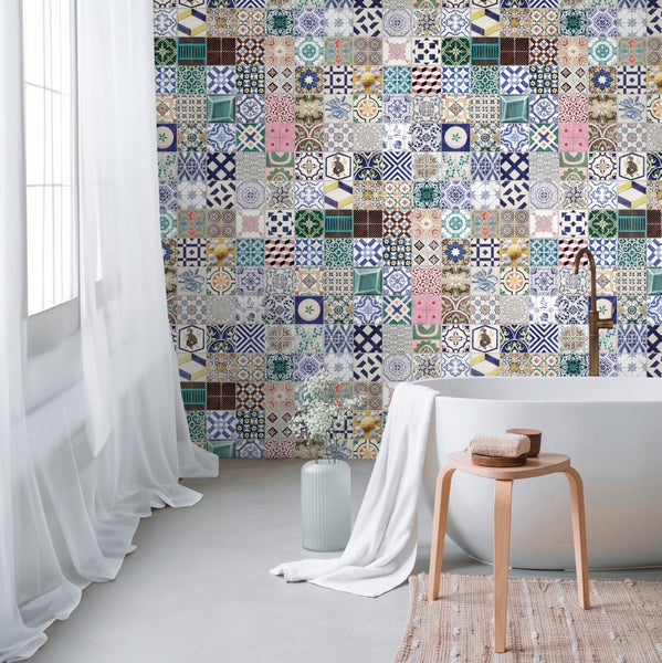Helles Badezimmer mit einer Wand aus bunten Patchwork Fliesen im Orient Design, einer freistehenden Badewanne und einem Holzhocker.
