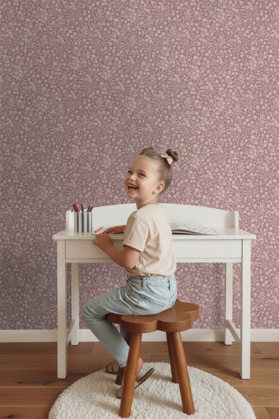 Kind sitzt an einem Schreibtisch vor einer floralen Tapete