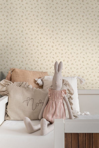 Vlies-Tapete mit feinem floralem Muster in einem hellen Kinderzimmer hinter einem Bett mit Kissen und einem Stoffhasen.