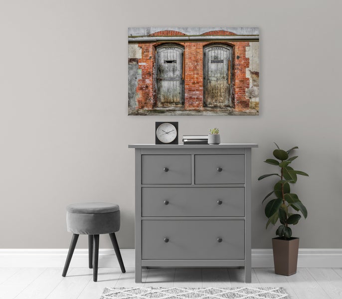 Wandbild mit Ziegelmauer und alten Türen über einer grauen Kommode mit Hocker und Pflanze in einem modern eingerichteten Raum.