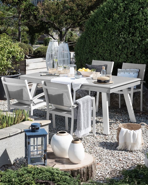 Gartenszene mit Esstisch, Stühlen, Dekoration und Pflanzen im Freien