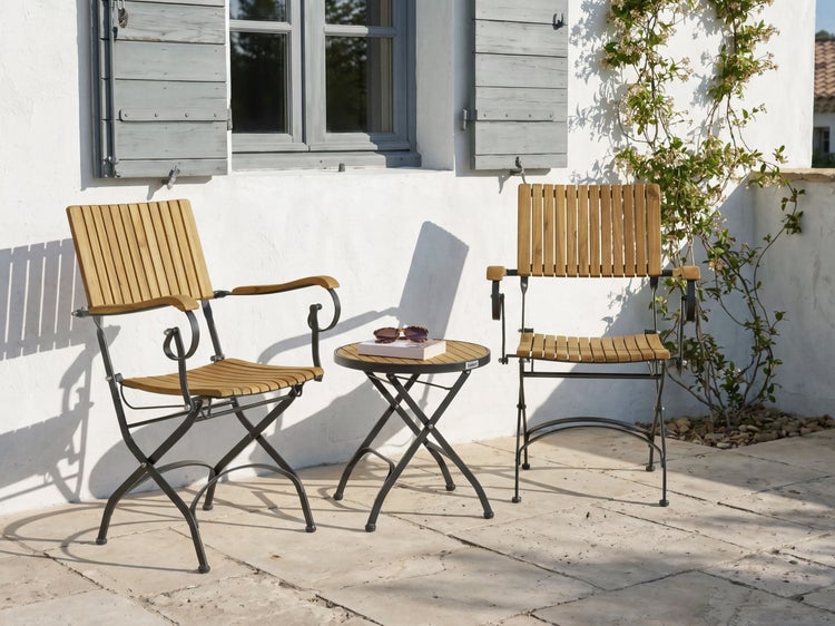 Gartenmöbel-Set aus zwei Armlehnenstühlen und einem runden Beistelltisch mit Holzlatten und Metallgestell auf einer hellen, sonnigen Terrasse.