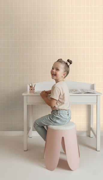 Mädchen sitzt an einem Schreibtisch vor einer Wand mit quadratischer Tapete