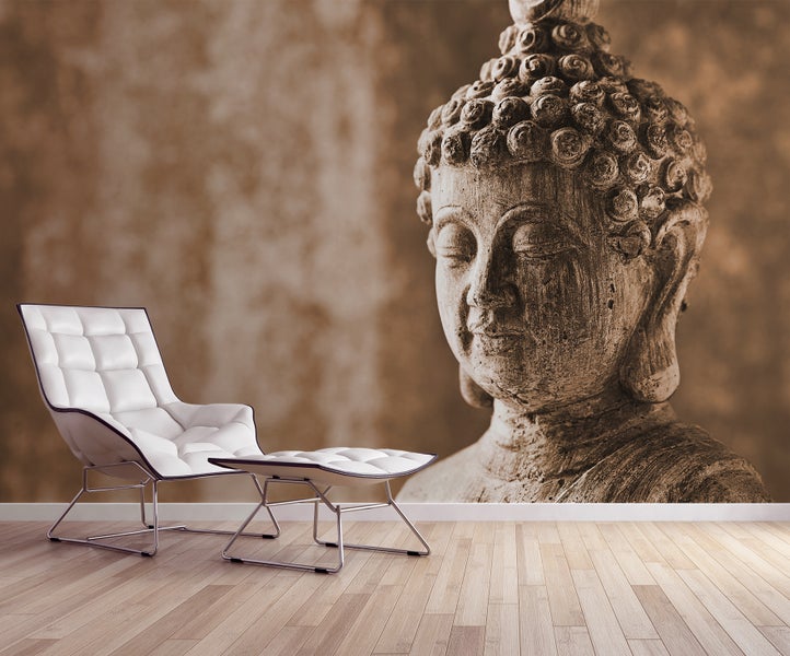Fototapete mit einem großen Buddha-Kopf aus Stein in einem modernen Wohnraum mit Parkettboden und weißem Sessel.