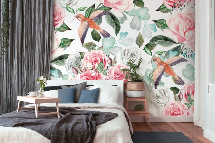 Schlafzimmer mit Wandtapete im Aquarellstil mit rosa Rosen und Vögeln sowie einem Bett mit Textilien in einem hellen Raum.