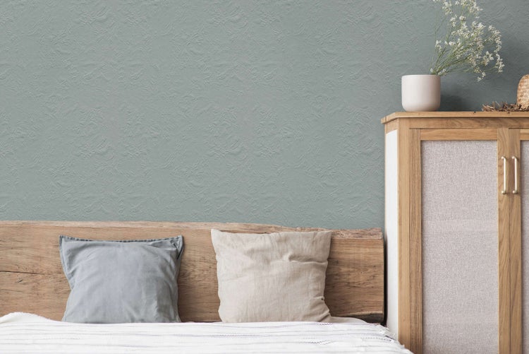 Strukturierte Wand in einem hellen Schlafzimmer mit einem Kopfteil aus Naturholz, Kissen und einem Holzschrank.