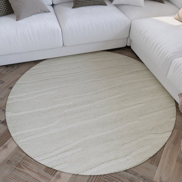 Runder Teppich mit dezenter Linienstruktur auf Parkettboden vor einem weißen Sofa in einem hellen Wohnzimmer.