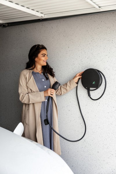 Eine Frau bedient eine runde, schwarze Wallbox mit Ladekabel und Stecker für Elektroautos in einer hellen Garage.