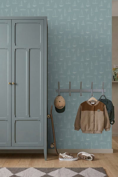 Organisiertes Kinderzimmer im nautischen Stil mit Segelboottapete, Schrank, Hakenleiste und hellem Holzboden.