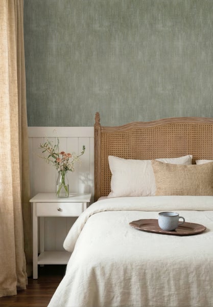 Helles Schlafzimmer mit strukturierter grüner Tapete, weißer Wandpaneele, Bett mit Rattankopfteil und weißem Nachttisch.