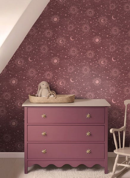 Vliestapete mit Sonnen, Monden und Sternen im Kinderzimmer hinter einer Kommode mit Sternengriffen.