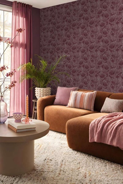 Wohnzimmer mit Blumenmuster-Tapete, braunem Sofa, rundem Couchtisch, Zimmerpflanze und Vorhängen in einer gemütlichen Inneneinrichtung.