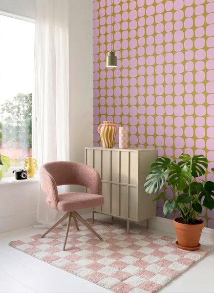 Modernes Zimmer mit Tapete in Rosa und Senfgelb mit Retromuster, einem beigen Schrank, rosa Sessel und einer Zimmerpflanze.