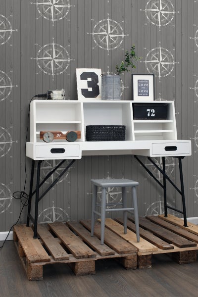 Schreibtisch mit Aufsatz, Hocker und Dekoration auf Europaletten vor einer Wand mit Kompassmuster