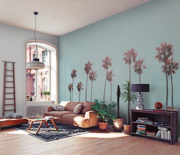 Helles Wohnzimmer mit Fototapete mit Palmen, braunem Ledersofa, Zimmerpflanzen und modernen Holzmöbeln auf Parkettboden.