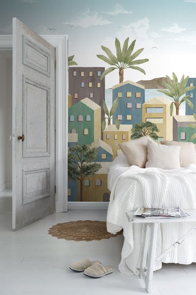 Helles Schlafzimmer mit Bett, Beistelltisch und einer Fototapete mit einem Küstenstadt-Motiv.