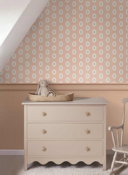 Tapete mit Blumenmuster in Ovalen über einer Kommode mit Sternenknöpfen und einem geflochtenen Korb in einem Kinderzimmer.