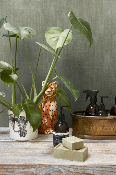 Dekorative Szene mit Zimmerpflanze, Tierfigur, Seife und Reinigungsflaschen auf einem Holztisch.