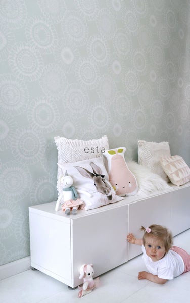 Helles Kinderzimmer mit gemusterter Tapete, weißem Sideboard und verschiedenen Stofftieren und Kissen