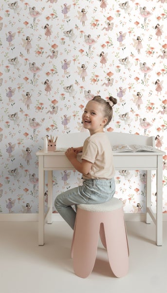 Mädchen sitzt an einem Schreibtisch vor einer Tapete mit Feen und Pilzen.