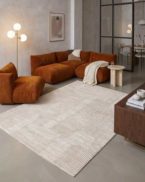 Modernes Wohnzimmer mit hellem Teppich mit Linienstruktur, modularem Cordsofa in Rostbraun, Stehlampe und minimalistischer Einrichtung.