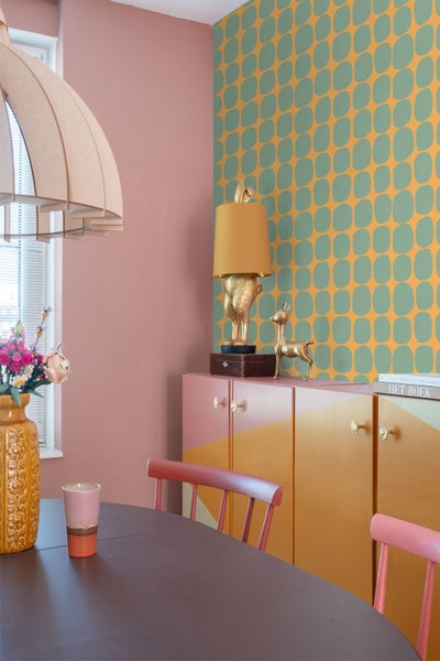 Retro-Einrichtung mit geometrisch gemusterter Tapete, einem farbig gestalteten Sideboard und einer Tischleuchte in Hasenform.