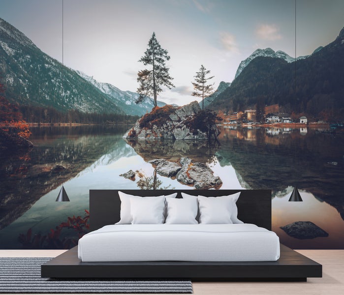 Modernes Schlafzimmer mit einer großflächigen Fototapete eines Bergsees mit Alpenpanorama, einem dunklen Holzbett und weißen Kissen.