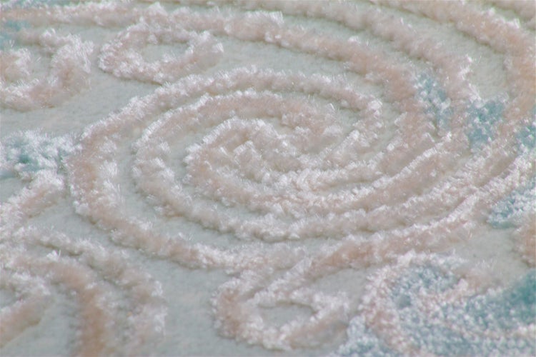 Nahaufnahme eines weichen Teppichs mit erhabenem Spiralmuster und flauschiger Hochflor-Struktur.