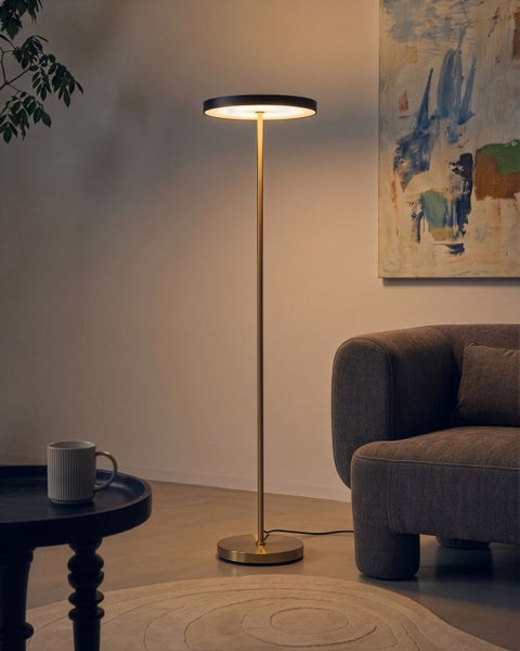 Moderne LED Stehlampe mit rundem Leuchtkopf und schlankem Metallständer in einem Wohnzimmer neben einem Sessel.