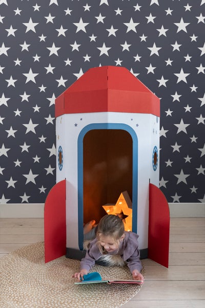 Mädchen liest in einem Pappraketen-Spielhaus auf einem runden Teppich