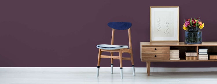 Moderne Wohnraumszene mit dunkelviolett gestrichener Wand, einem Holzstuhl und einem niedrigen Sideboard aus Holz vor hellem Boden.